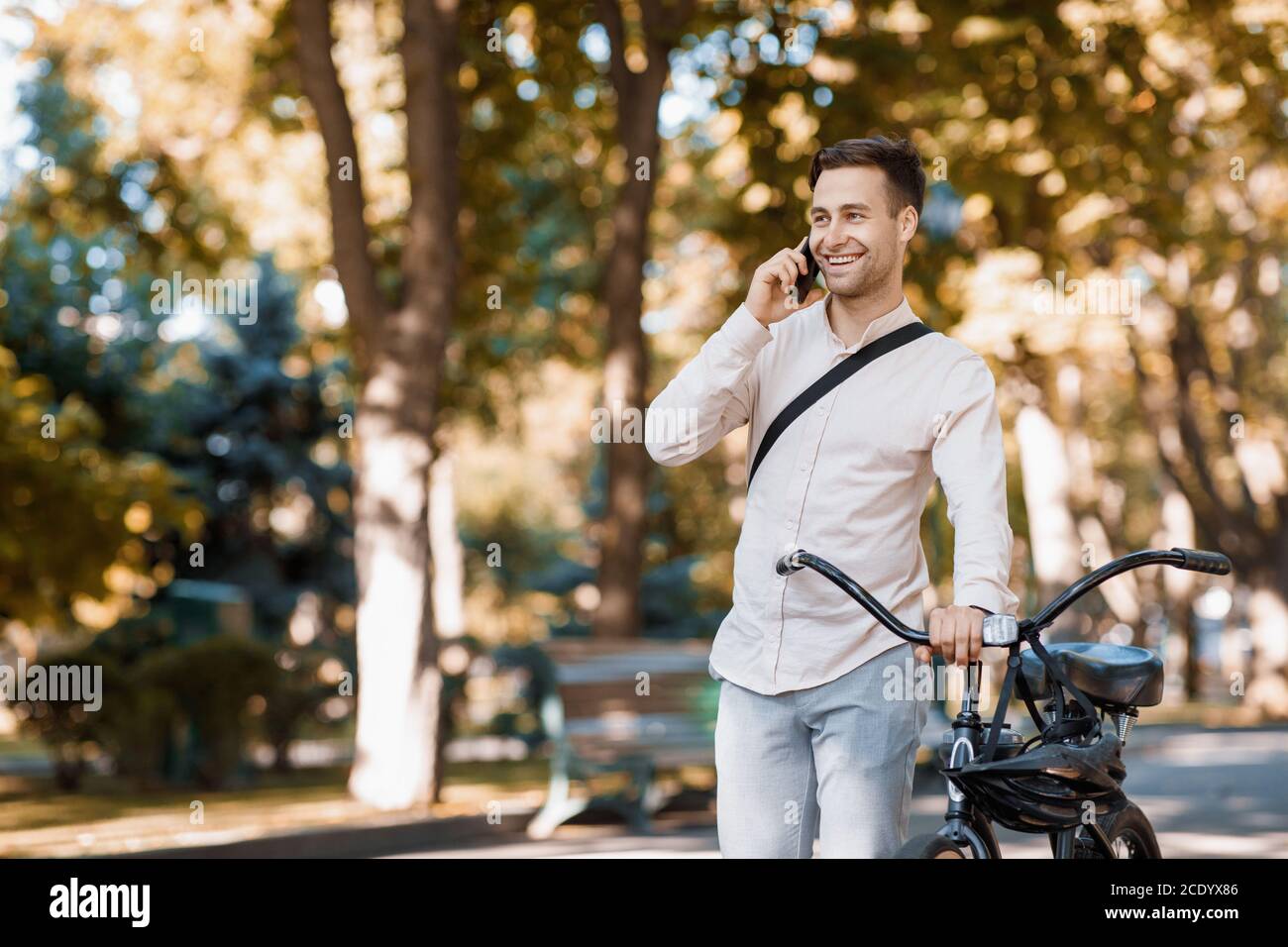 Route pour travailler sur le transport écologique. Guy marche avec téléphone dans le parc avec vélo Banque D'Images