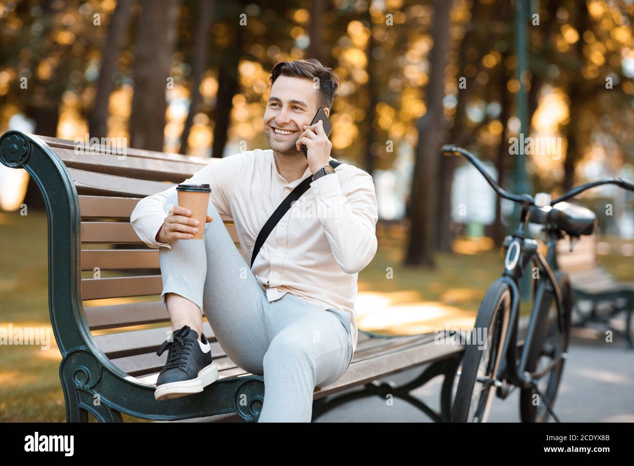 Pause déjeuner au travail à l'extérieur. Boire du café et parler au téléphone portable sur le banc dans le parc avec vélo Banque D'Images