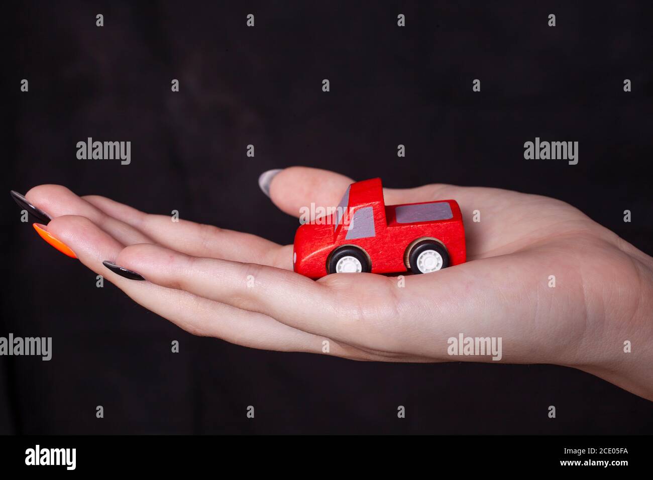 Main de la femme tenant la voiture miniature contre un fond noir Banque D'Images
