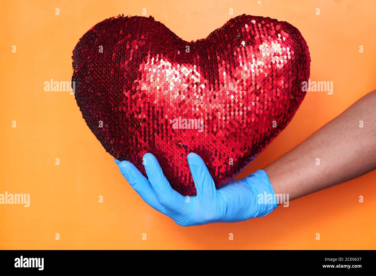 Main du médecin dans des gants médicaux tenant le cœur rouge. Banque D'Images