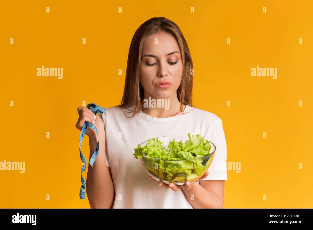 Perte de poids. Jeune femme pensive avec ruban de mesure et bol à salade de laitue Banque D'Images