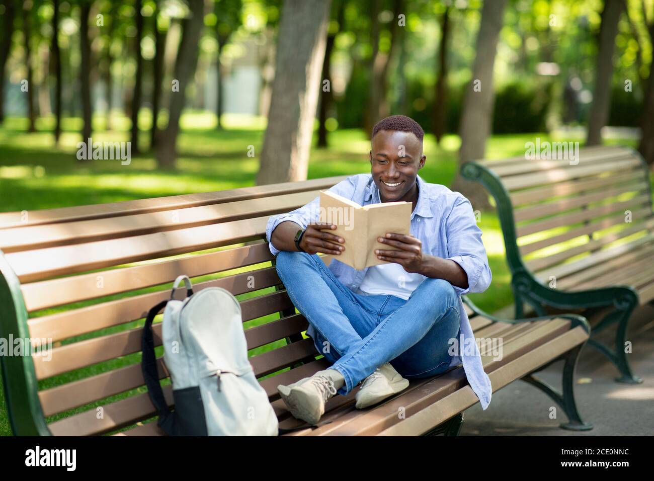 Positif noir gars lisant un livre intéressant sur banc au parc d'été, espace de copie Banque D'Images