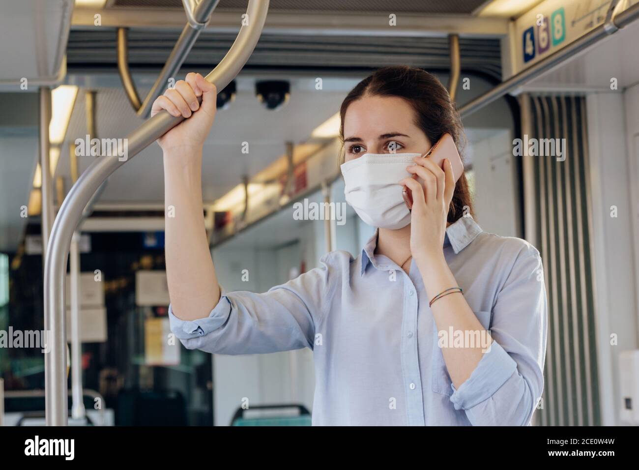 Photo d'une jeune femme portant un masque parler au téléphone en étant debout sur le tram Banque D'Images