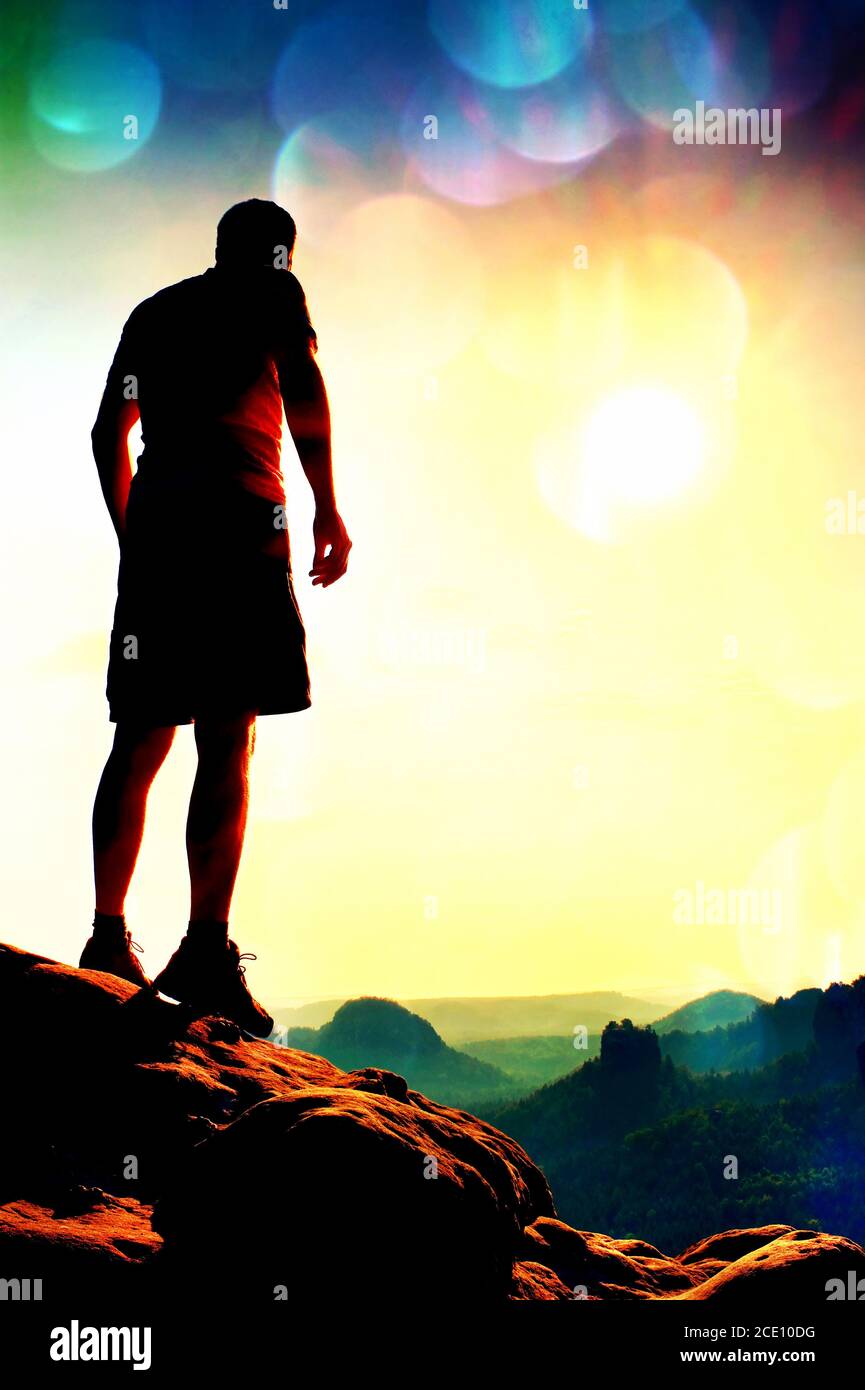 Grain du film. Slim touriste dans le pantalon sur la falaise de l'empire de roche est regarder vers le bas de la vallée du matin. Soleil chaud au-dessus. Banque D'Images