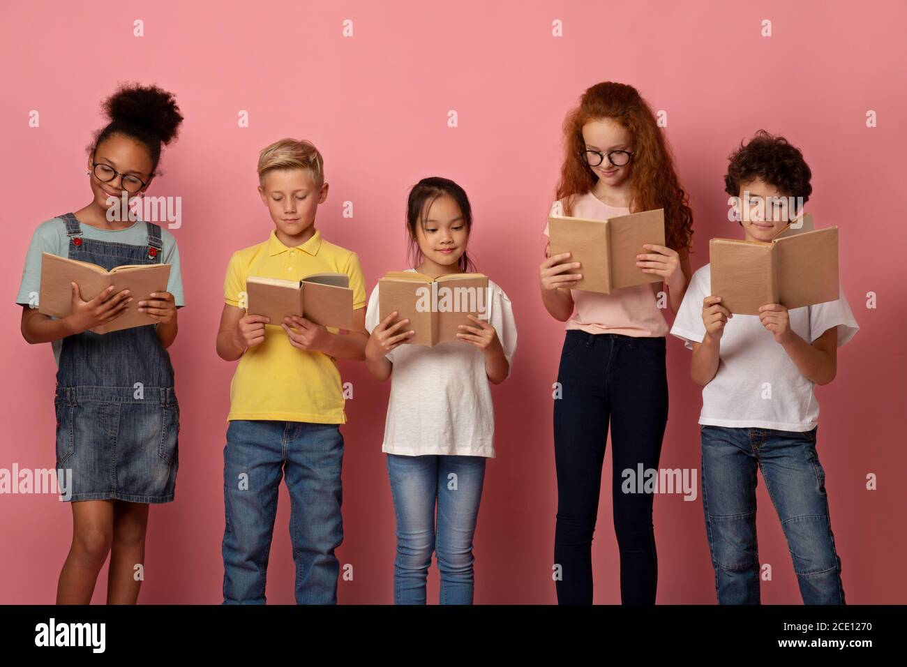 Des élèves diligents de différentes races lisant des livres ensemble sur le rose arrière-plan Banque D'Images