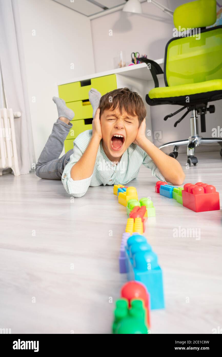 Un garçon autiste a mis des jouets dans une rangée sur le crier le sol et couvrir les oreilles avec les mains Banque D'Images