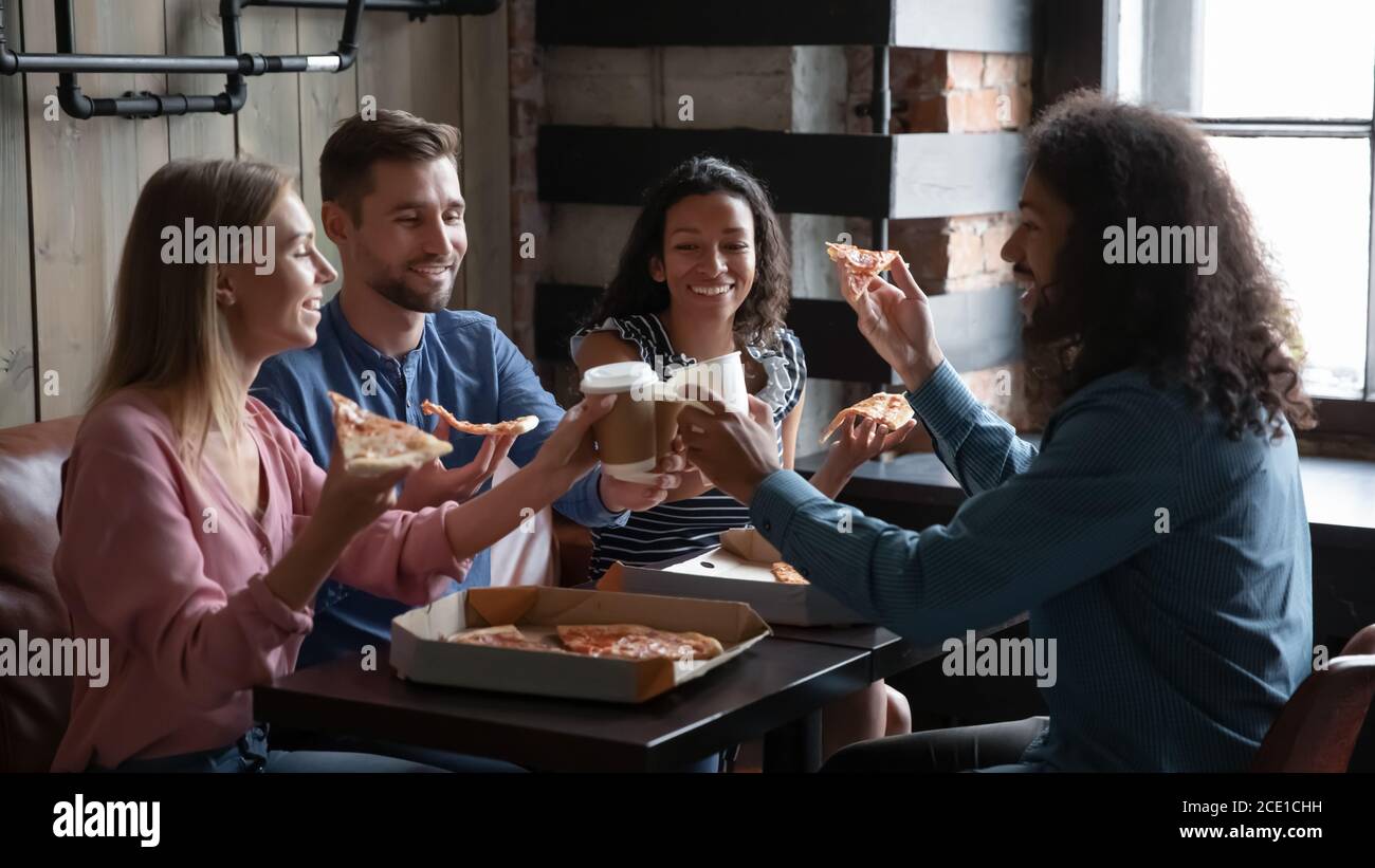 Des amis heureux et variés qui mangent de la pizza et s'amusent au café Banque D'Images