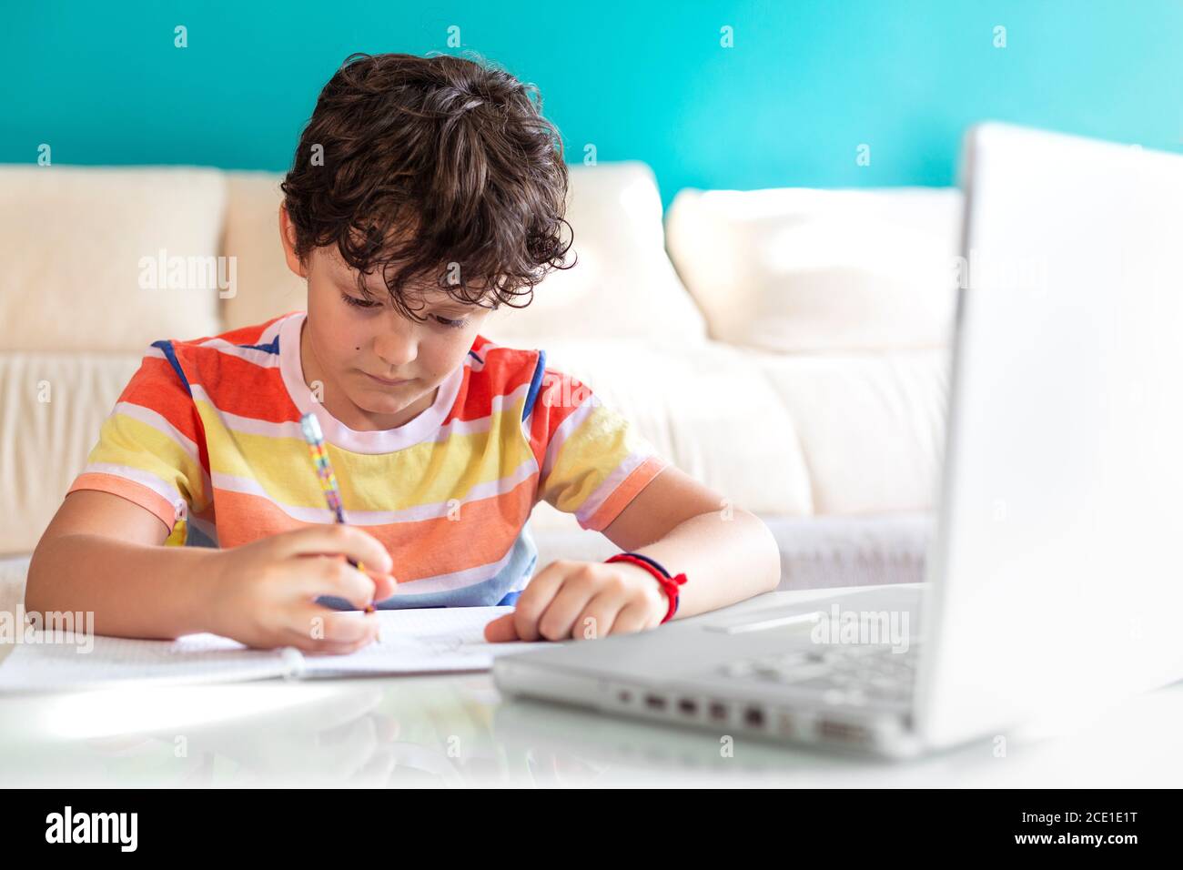 Un petit garçon fait ses devoirs devant un ordinateur portable. Concept de l'éducation en ligne à partir de la maison. Banque D'Images