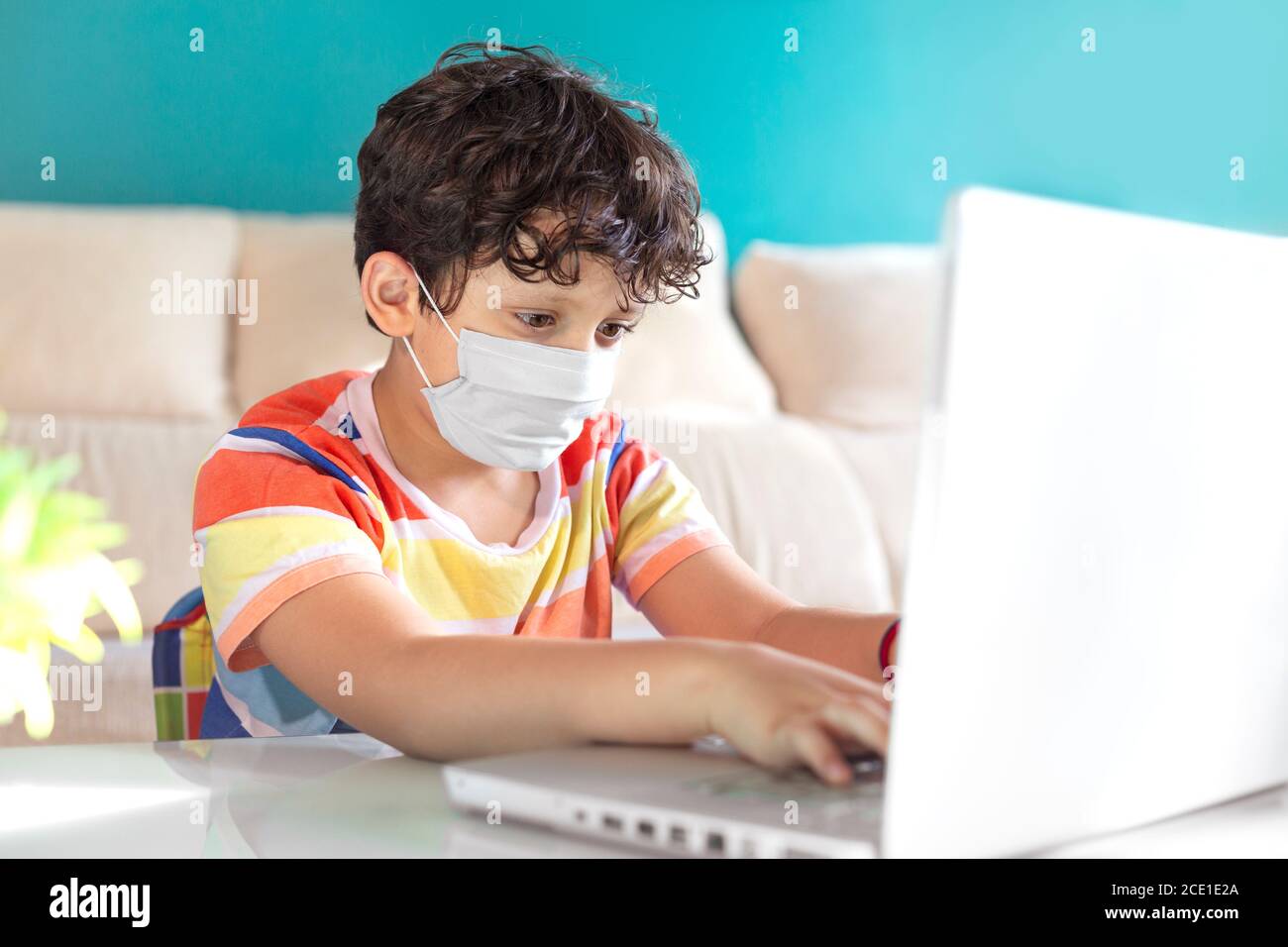 Petit garçon utilisant un ordinateur portable pour étudier de la maison. Il porte un masque. Concept de l'éducation en ligne. Banque D'Images