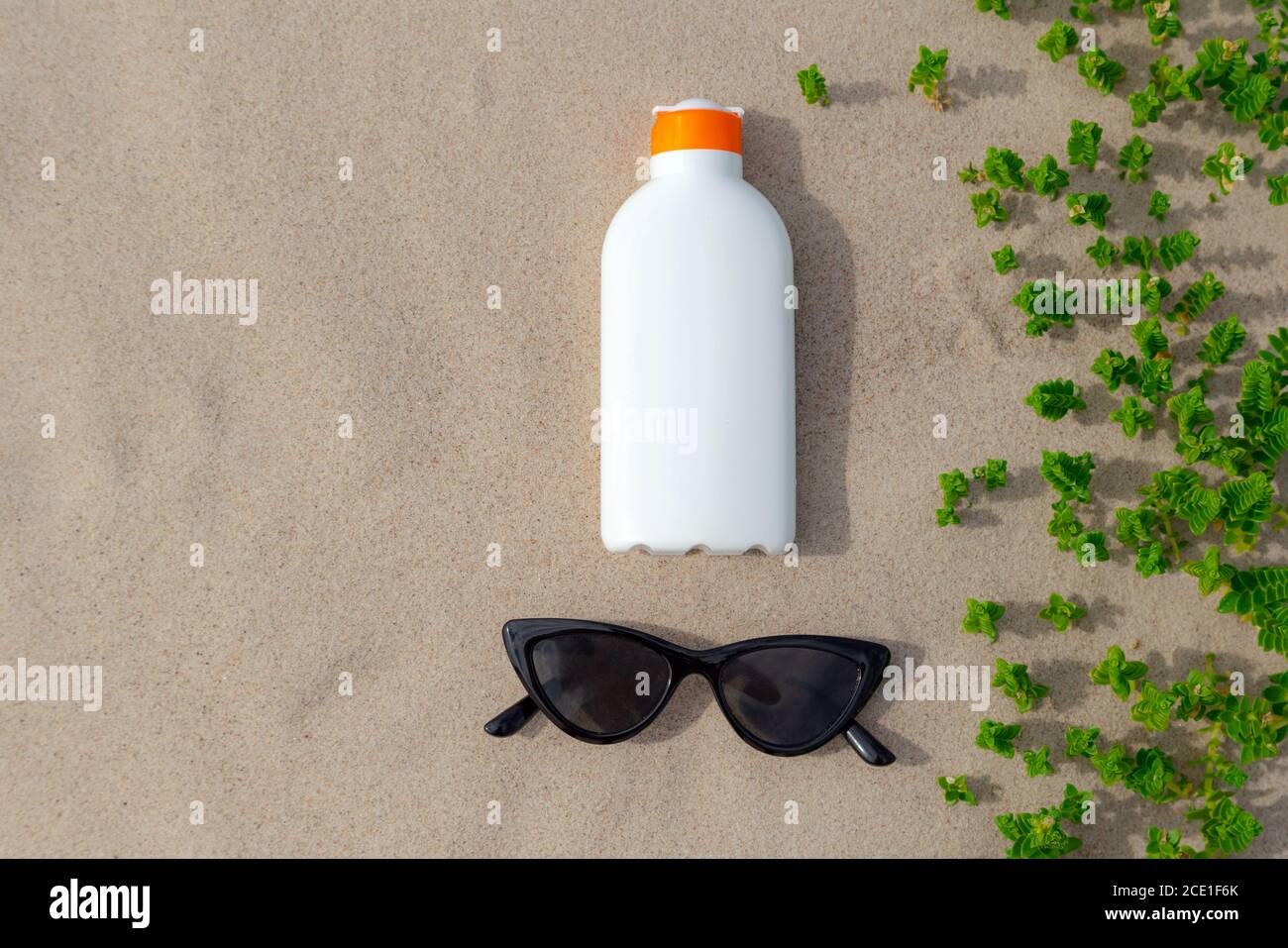 Lotion de protection solaire et lunettes de soleil dans le sable lors d'une journée ensoleillée à la plage. Bouteille de protection crème blanche contre les coups de soleil. Personne. Banque D'Images