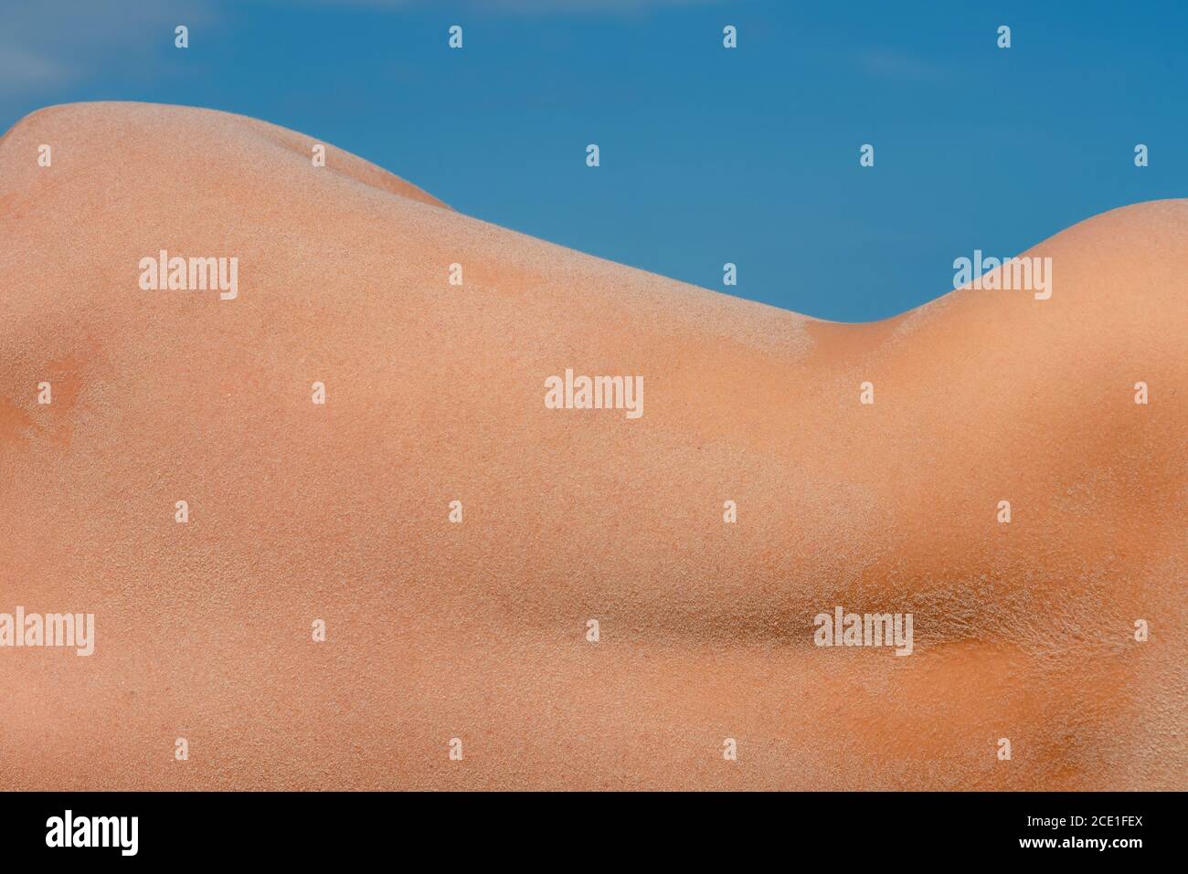 Dos d'homme de sable sur la plage par une journée ensoleillée. Courbe sablonneuse des hanches athlétiques de l'homme. Arrière-plan bleu ciel. Banque D'Images