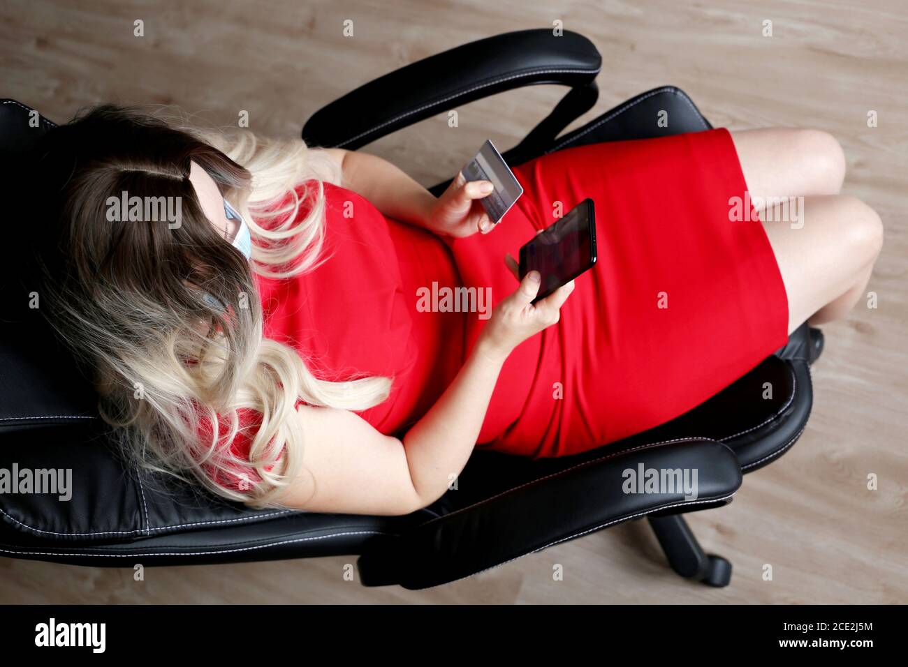 Femme dans le masque de visage assis dans la chaise de bureau avec carte de crédit et téléphone mobile dans les mains. Concept d'achat et de paiement en ligne Banque D'Images