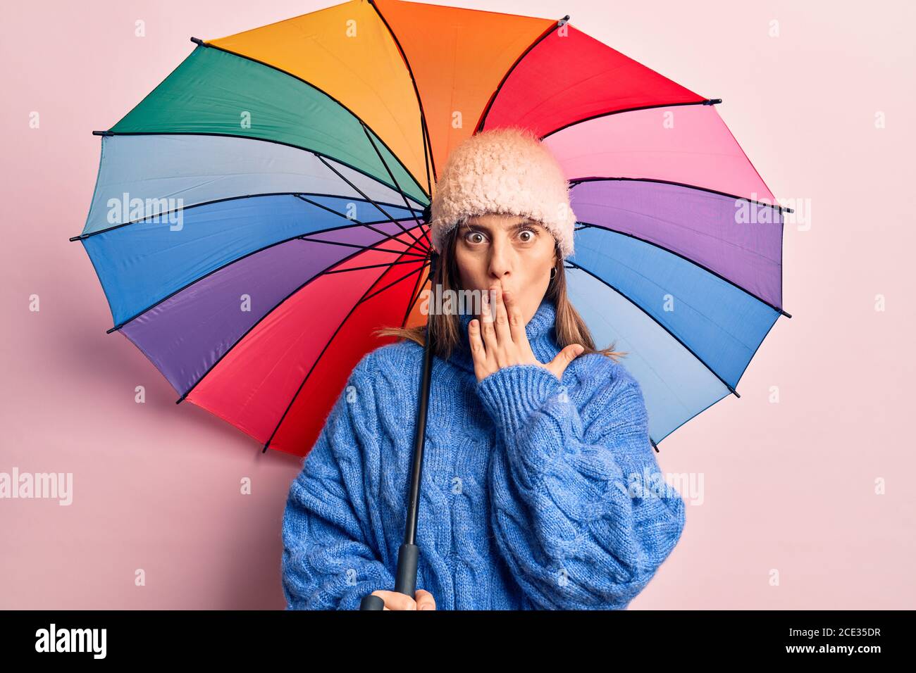 Jeune belle femme tenant un parapluie coloré couvrant la bouche avec la  main, choqué et peur de l'erreur. Expression surprise Photo Stock - Alamy