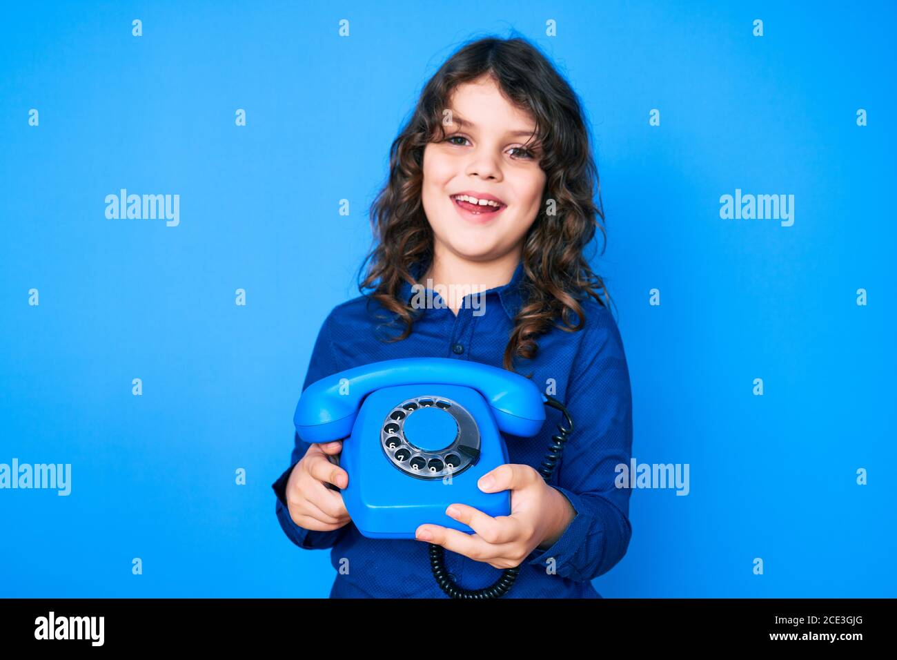 Mignon petit garçon hispanique avec de longs cheveux tenant le téléphone vintage souriant et riant fort parce que drôle de blague fou. Banque D'Images