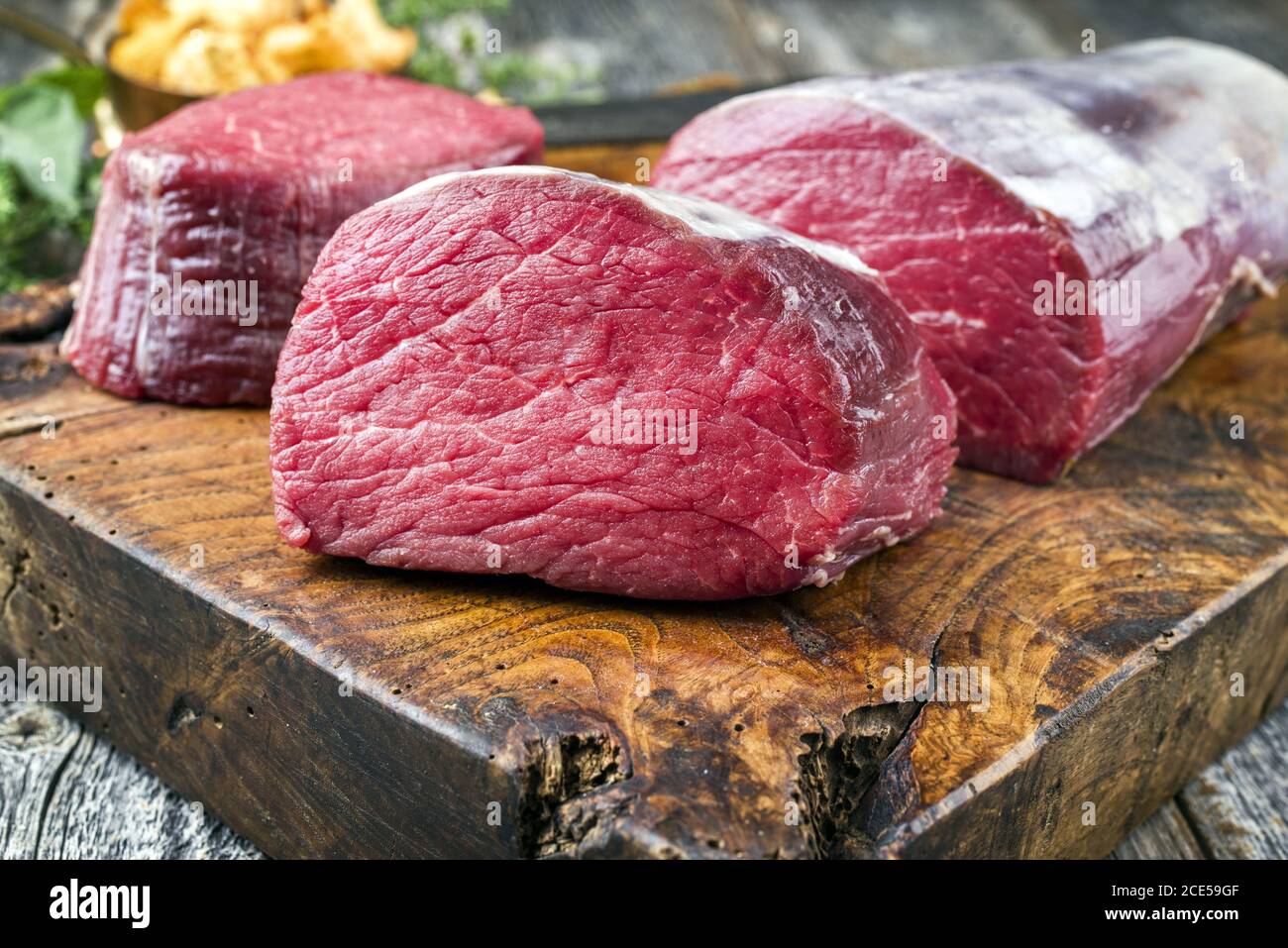 Filet de bœuf vieilli sec, steak naturel comme en gros plan avec des chanterelles sur une planche à découper en bois Banque D'Images