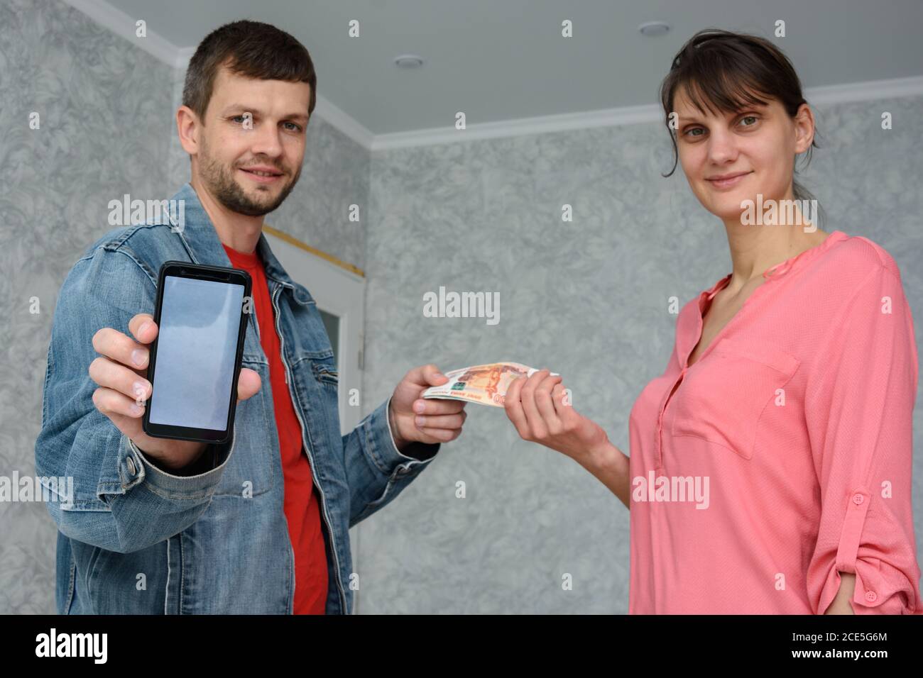 Un travailleur indépendant reçoit de l'argent d'une fille pour réparer une chambre et montre un téléphone avec l'application mobile Banque D'Images