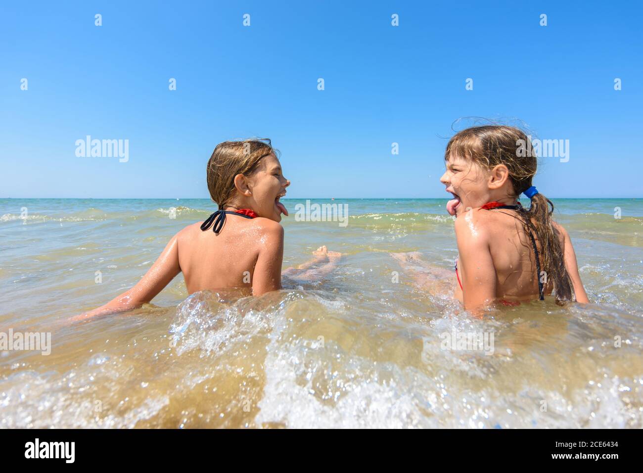 Les enfants s'assoient ensemble dans des eaux peu profondes et se montrent l'une l'autre langue Banque D'Images