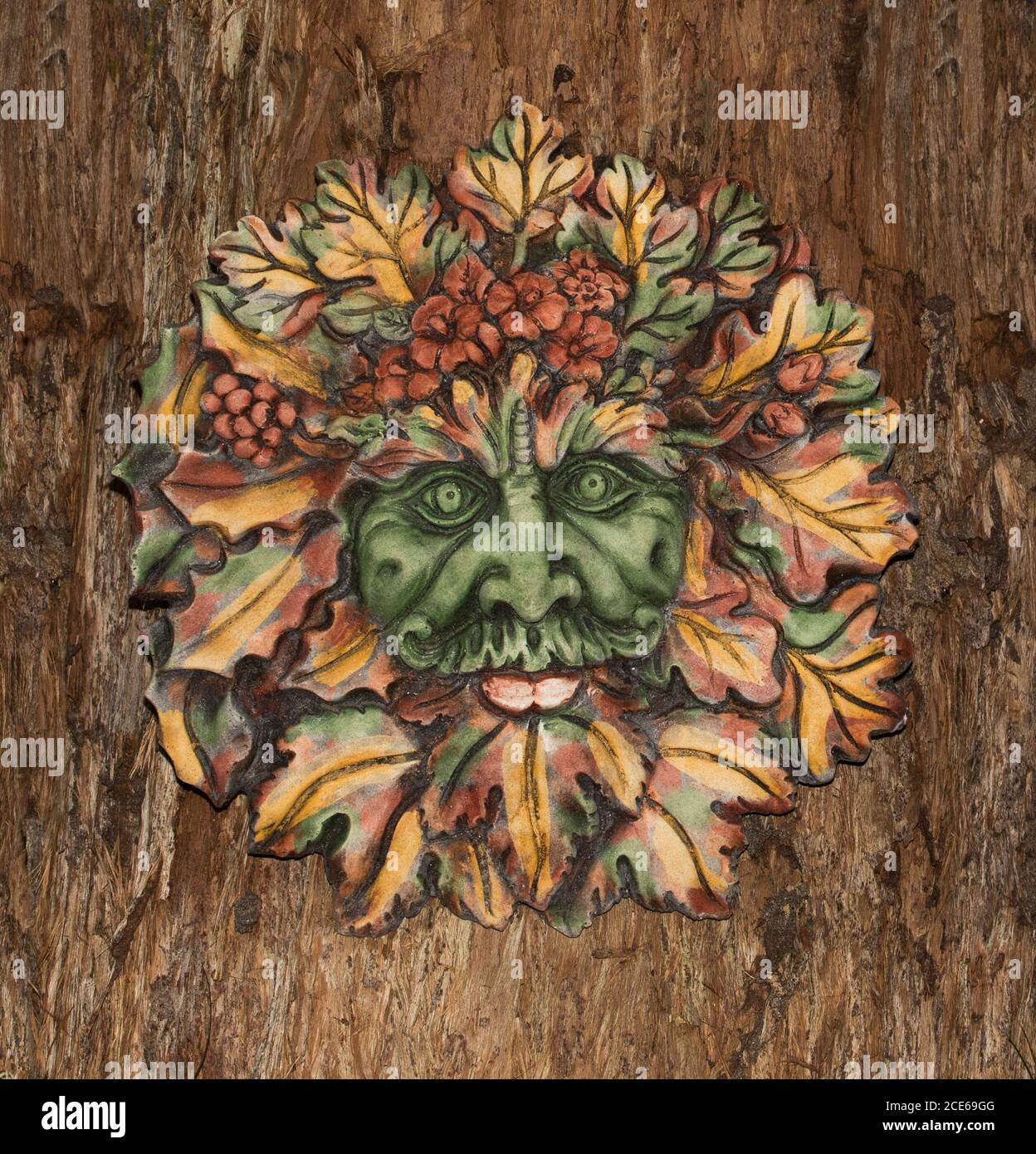 Art de jardin en béton très décoratif, face des feuilles d'automne de Green Man, esprit mythique britannique des forêts, sur fond d'écorce d'arbre brun Banque D'Images