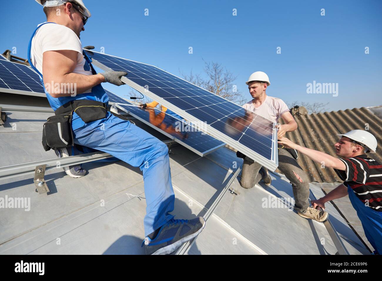 Les ingénieurs de l'équipe masculine installent un système autonome de panneaux photovoltaïques solaires. Électriciens soulevant module solaire bleu sur le toit de la maison moderne. Énergie alternative concept écologique. Banque D'Images