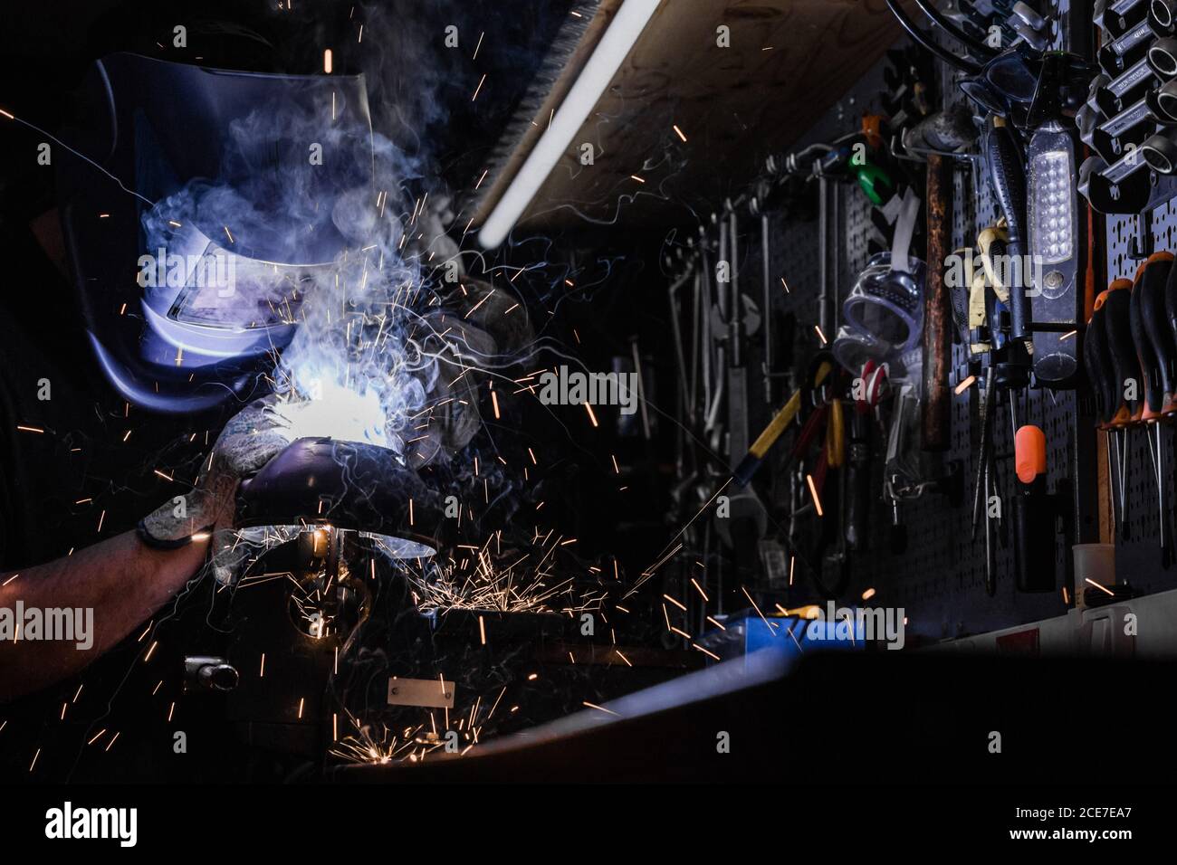 Vue latérale d'un travailleur anonyme debout sur un casque de protection sur établi et fixation des détails métalliques à l'aide d'un outil de soudage Banque D'Images