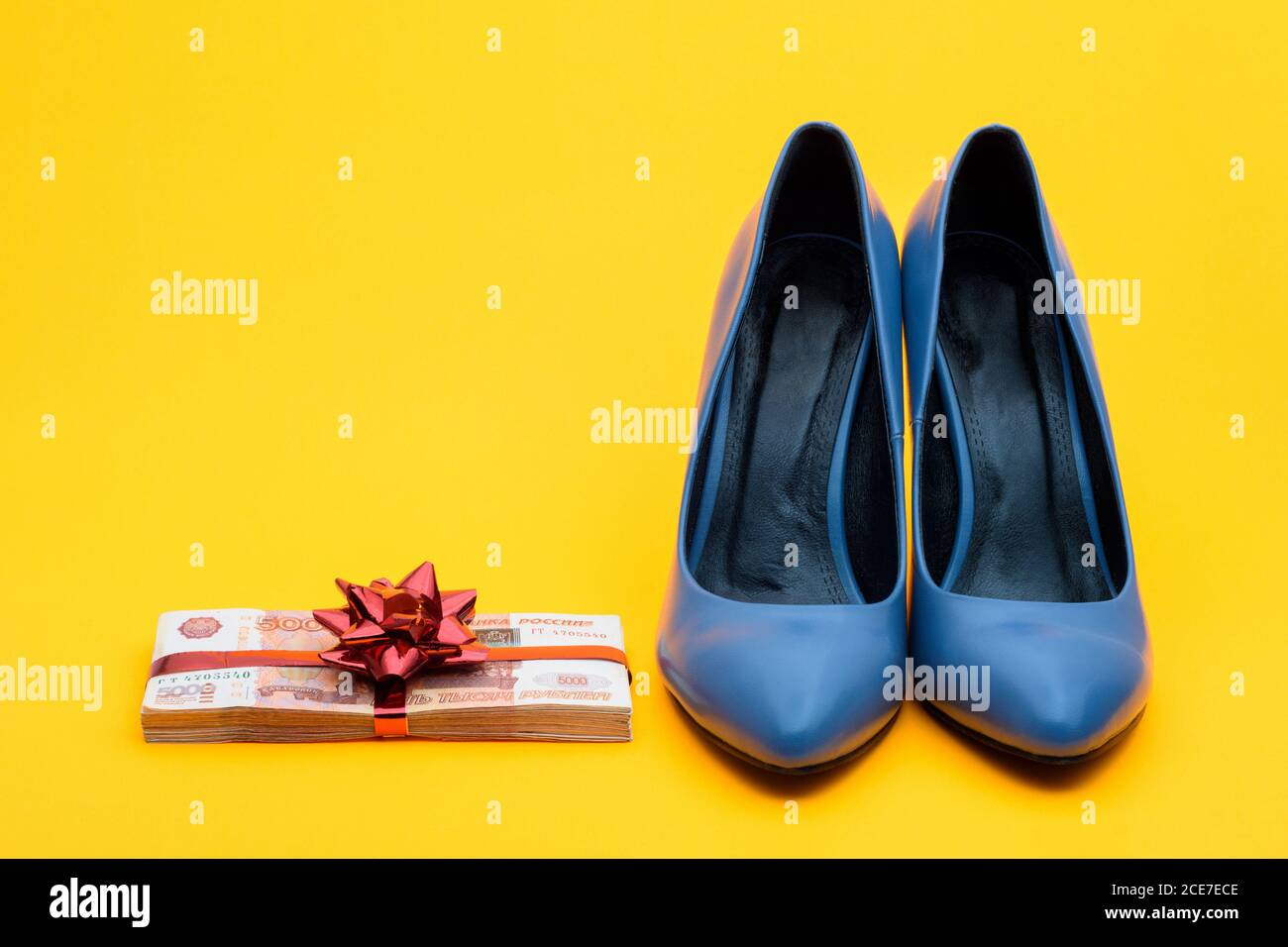 De belles chaussures pour femmes et une grande somme d'argent avec un ruban cadeau sur fond jaune Banque D'Images