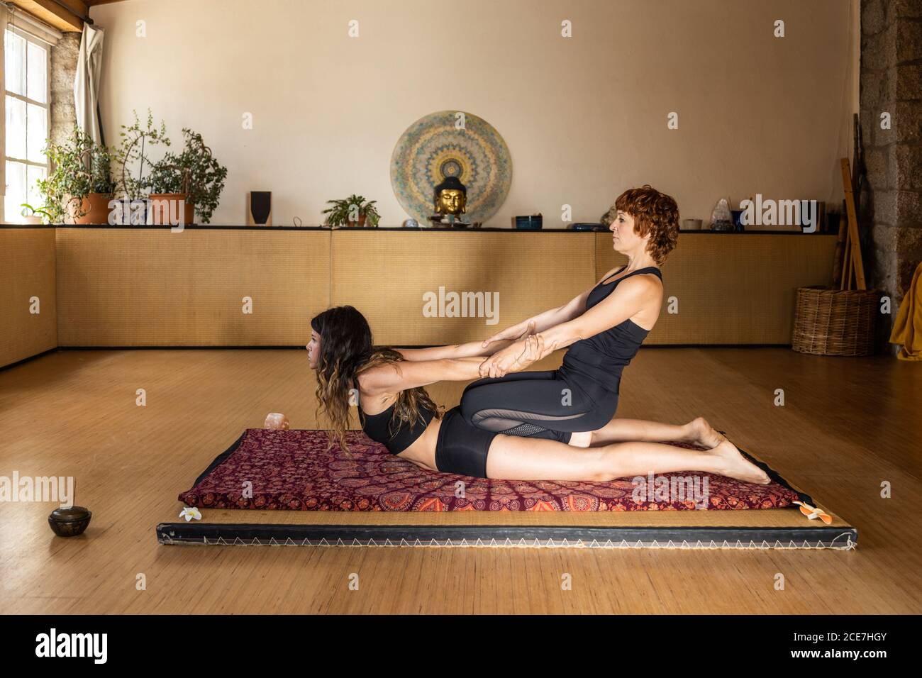Vue latérale des femmes flexibles dans les vêtements de sport de Cobra et Pose de chaise tenant les mains et faisant de l'acro yoga en studio Banque D'Images