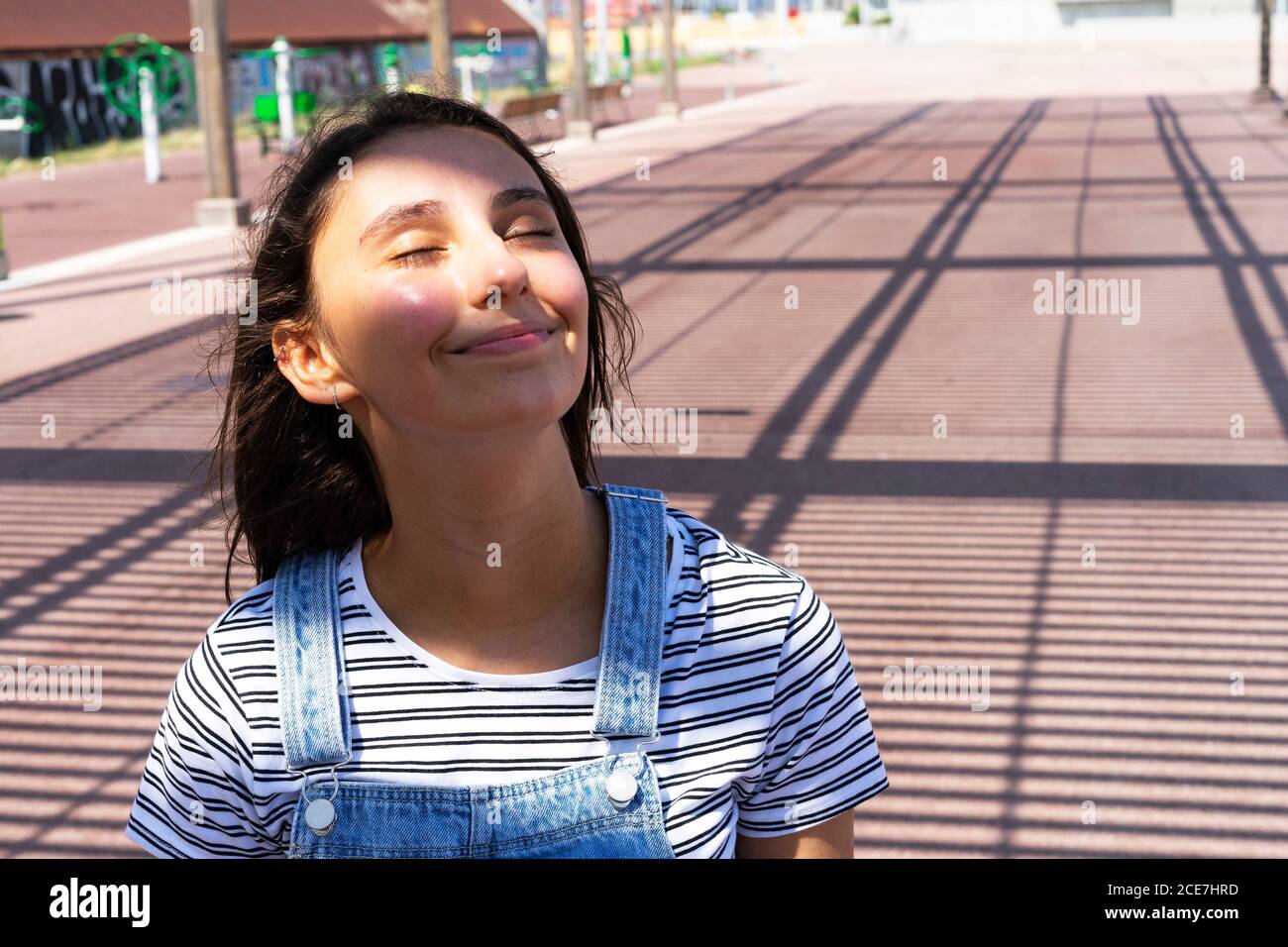 Adolescent ravi de fermer les yeux et de sourire tout en se reposant sur la ville rue par beau temps Banque D'Images