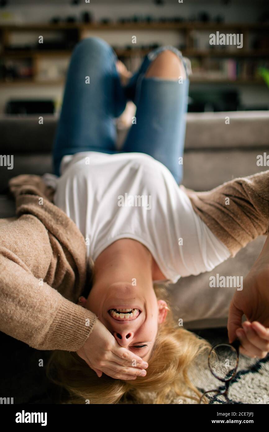 Femme gaie dans des vêtements décontractés se détendant sur un canapé confortable salon et rire à blague avec les yeux fermés Banque D'Images