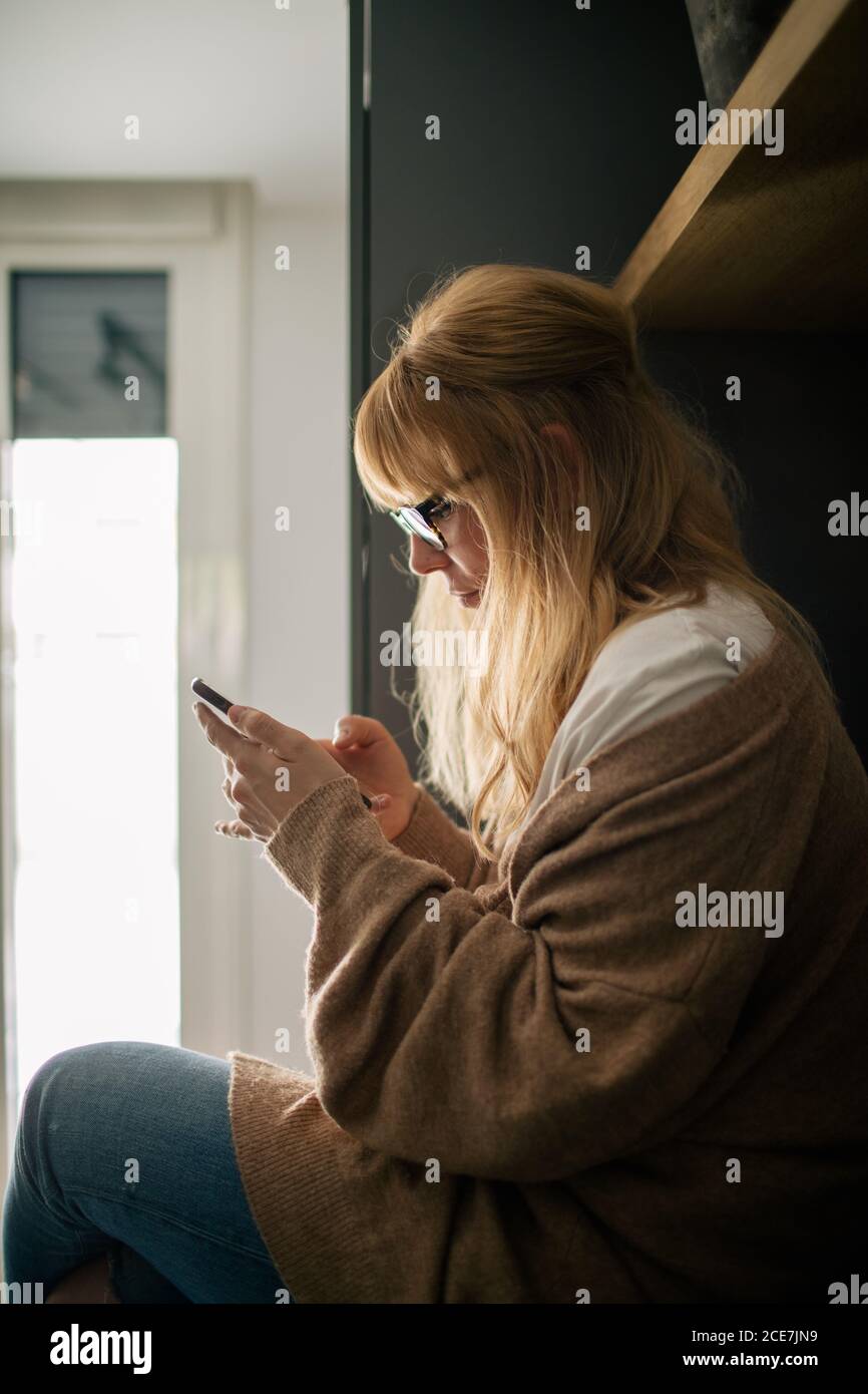 Vue latérale d'une femme sereine dans des vêtements confortables comptoir dans la cuisine et lecture de messages sur les médias sociaux Banque D'Images