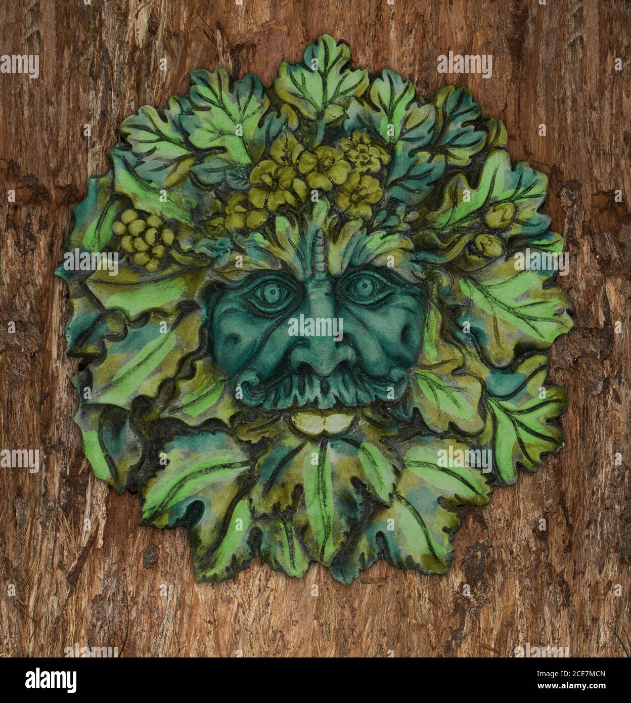 Art de jardin en béton très décoratif, face de feuilles de Green Man, esprit mythique britannique des forêts, sur fond d'écorce d'arbre brun Banque D'Images
