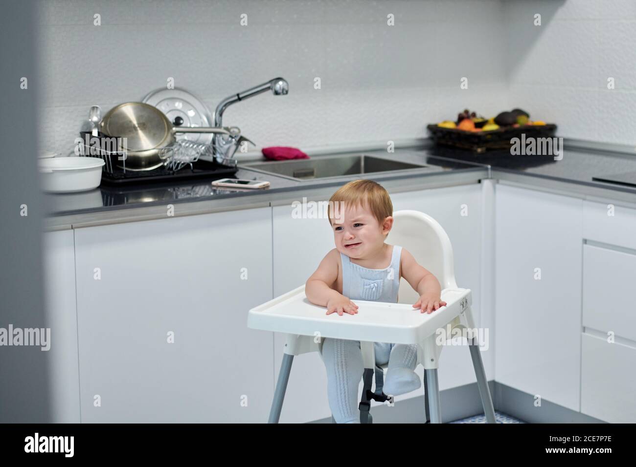 Mignon gai enfant assis dans une chaise haute et manger sucré raisins frais dans la cuisine maison Banque D'Images