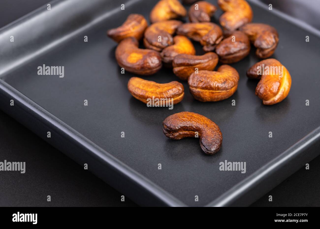 Les noix de cajou sont rôties jusqu'à ce qu'elles soient brûlées trop cuites au goût noir et brun foncé, trop amères et difficiles à manger sur une assiette noire. Banque D'Images