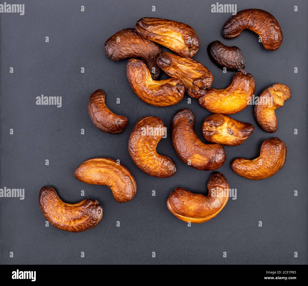 Les noix de cajou sont rôties jusqu'à ce qu'elles soient brûlées trop cuites au goût noir et brun foncé, trop amères et difficiles à manger sur une assiette noire. Banque D'Images