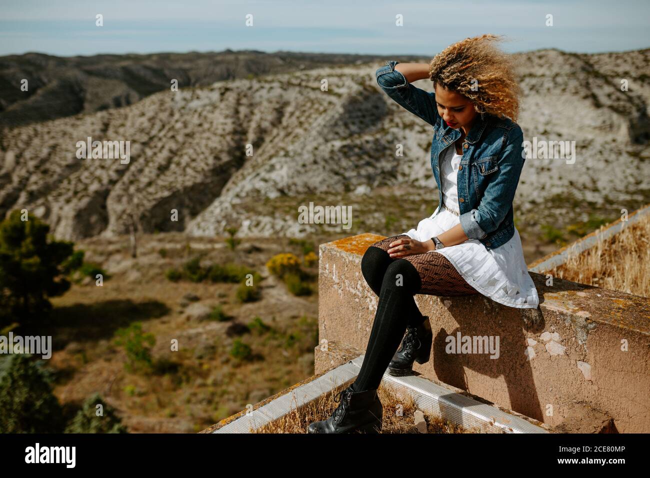 Vue latérale d'une femme afro-américaine assise sur le bord de vieux bâtiment et paysage étonnant en été Banque D'Images