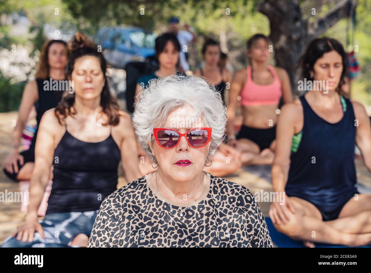 La femme mûre concentrée dans le lotus pose méditant tout en pratiquant le yoga en plein air assis sur un podium en bois Banque D'Images