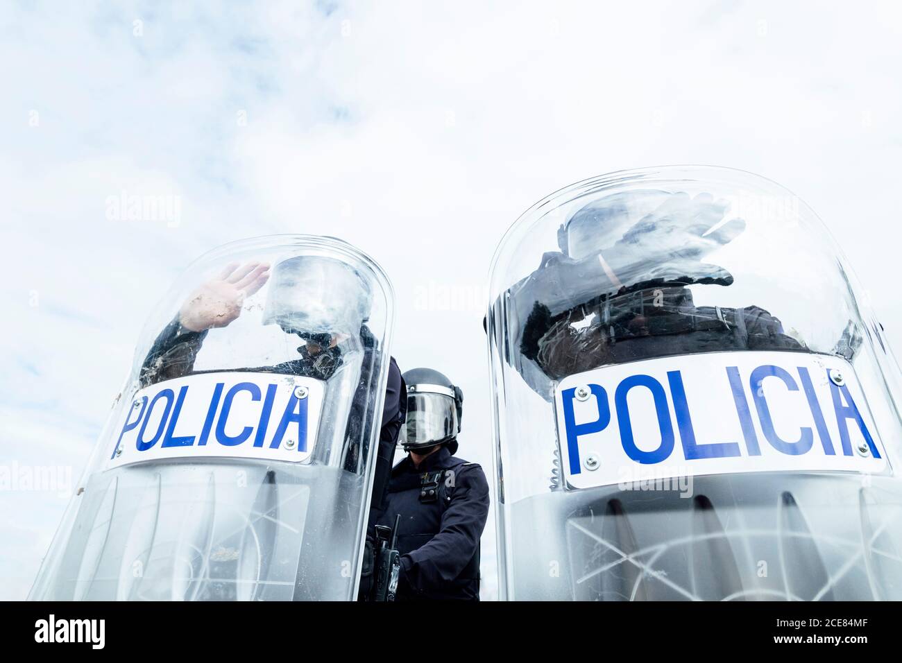 Faible angle des soldats de police anonymes dans les uniformes de protection et casques se tenant contre une fourgonnette et se défendant par des boucliers anti-émeute Banque D'Images