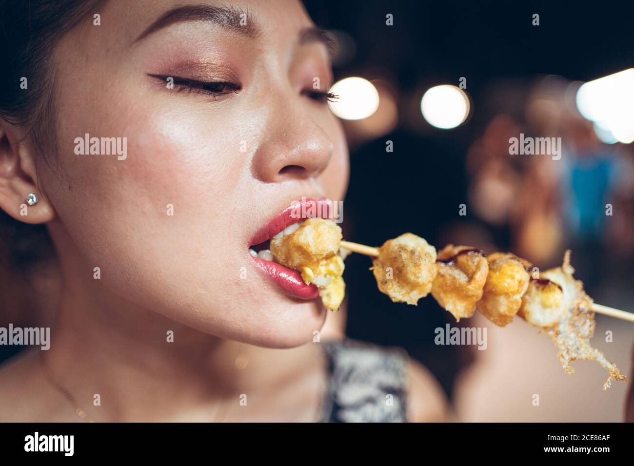 Contenu asiatique femme mangeant délicieux œufs de caille frits sur bâton En vous tenant au marché nocturne de Zhubei Banque D'Images