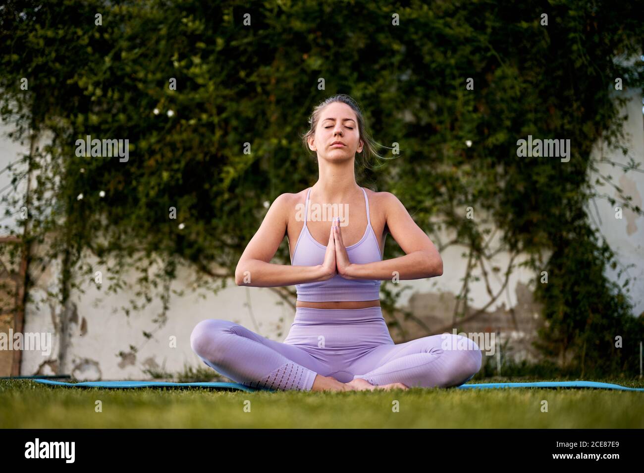 Femme paisible en tenue active assise à Padmasana avec Namaste geste tout en méditant et en pratiquant le yoga sur la pelouse Banque D'Images