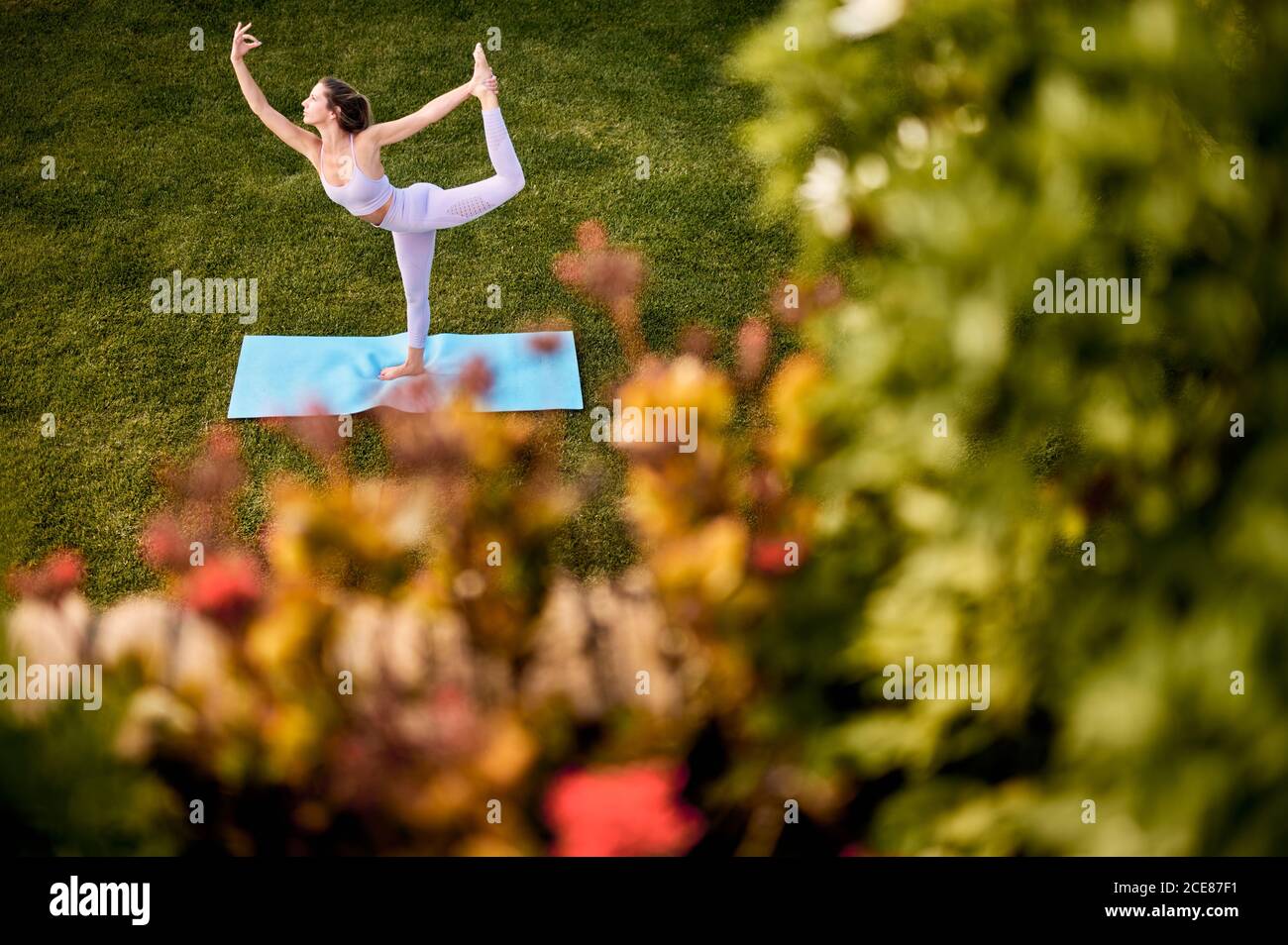 Vue du dessus de la femme mince dans l'équilibre de sportswear Sur la jambe à Natarajasana tout en pratiquant le yoga sur la pelouse verte dans le parc Banque D'Images