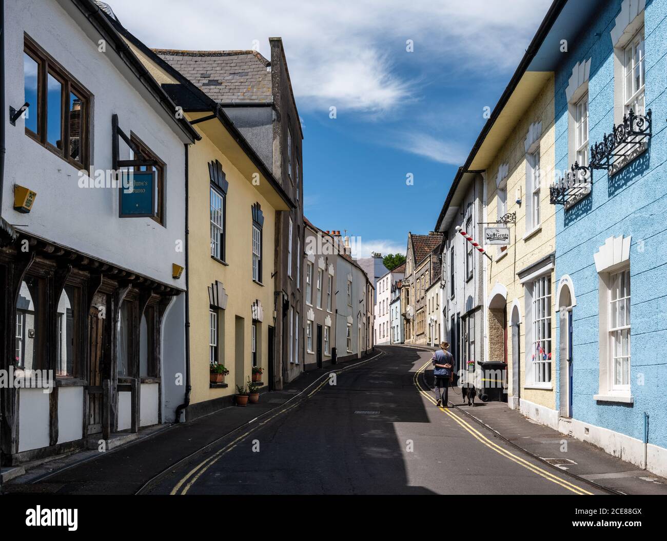 Un homme marche un chien à côté des boutiques traditionnelles et des vieilles maisons colorées sur Axbridge High Street dans Somerset. Banque D'Images