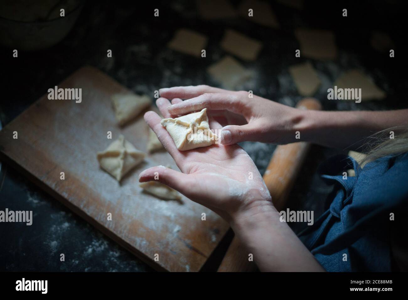De dessus de la récolte anonyme femme préparant des boulettes carrées similaires avec décoration sur le dessus de la planche à découper avec de la farine près de la broche en bois Banque D'Images