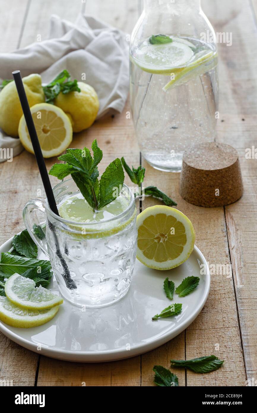 Boisson rafraîchissante froide avec soda et citron garni feuilles de menthe fraîche servies sur une tasse en verre avec de la paille table en bois Banque D'Images