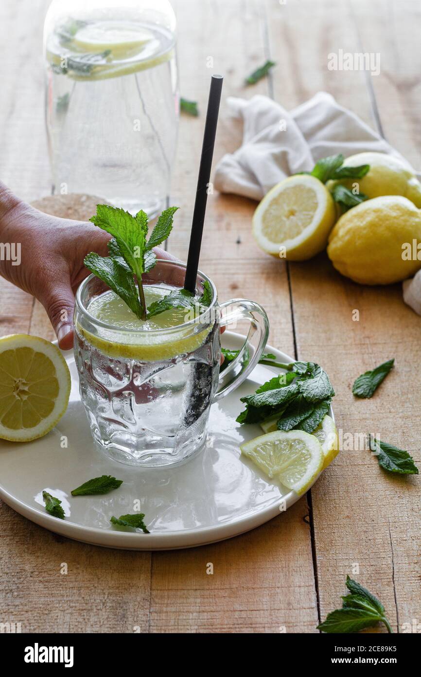 Croissent les personnes méconnaissables en prenant une tasse de verre de la citronnade froide savoureuse avec de l'eau sodée et des feuilles de menthe placées sur une table en bois Banque D'Images