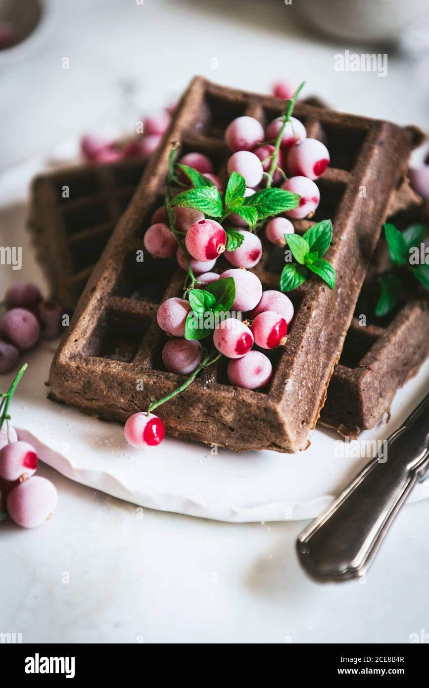 Des gaufres savoureuses au chocolat aux flocons d'avoine avec baies de gooseberries sont servies sur plaque blanche avec cuillère et couteau sur bois clair tableau Banque D'Images