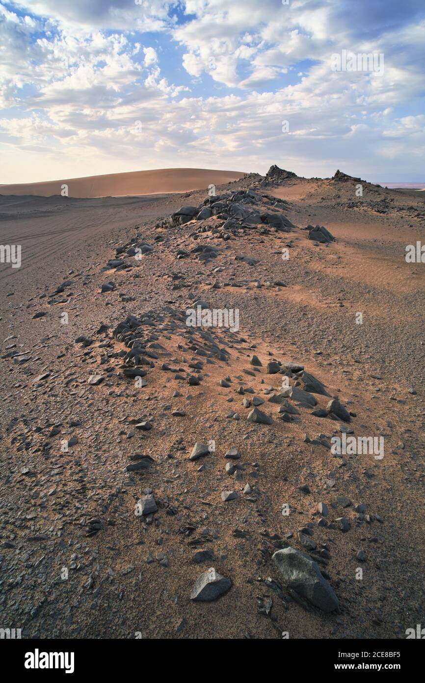 Vue sur le paysage du désert avec des dunes de sable et des pierres sans forme avec une surface en rade sous un ciel pittoresque avec des nuages l'après-midi Banque D'Images