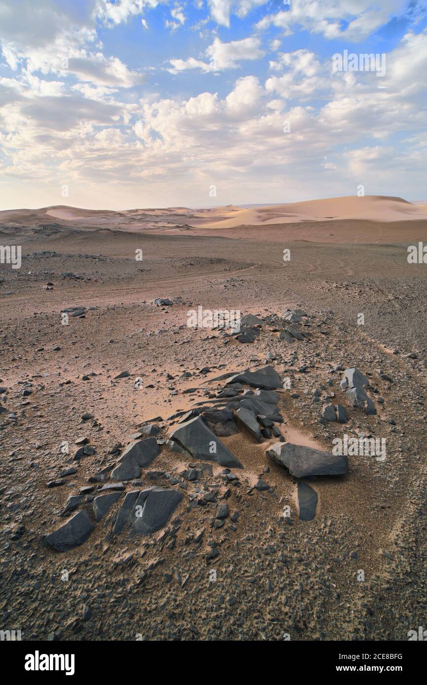 Vue sur le paysage du désert avec des dunes de sable et des pierres sans forme avec une surface en rade sous un ciel pittoresque avec des nuages l'après-midi Banque D'Images