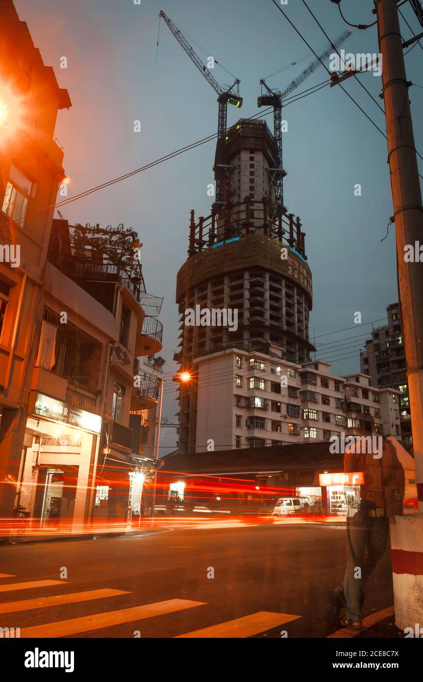 Bas angle de gratte-ciel contemporain en construction avec grues contre Ciel nocturne sur la rue illuminée de la ville de Xiamen en Chine Banque D'Images