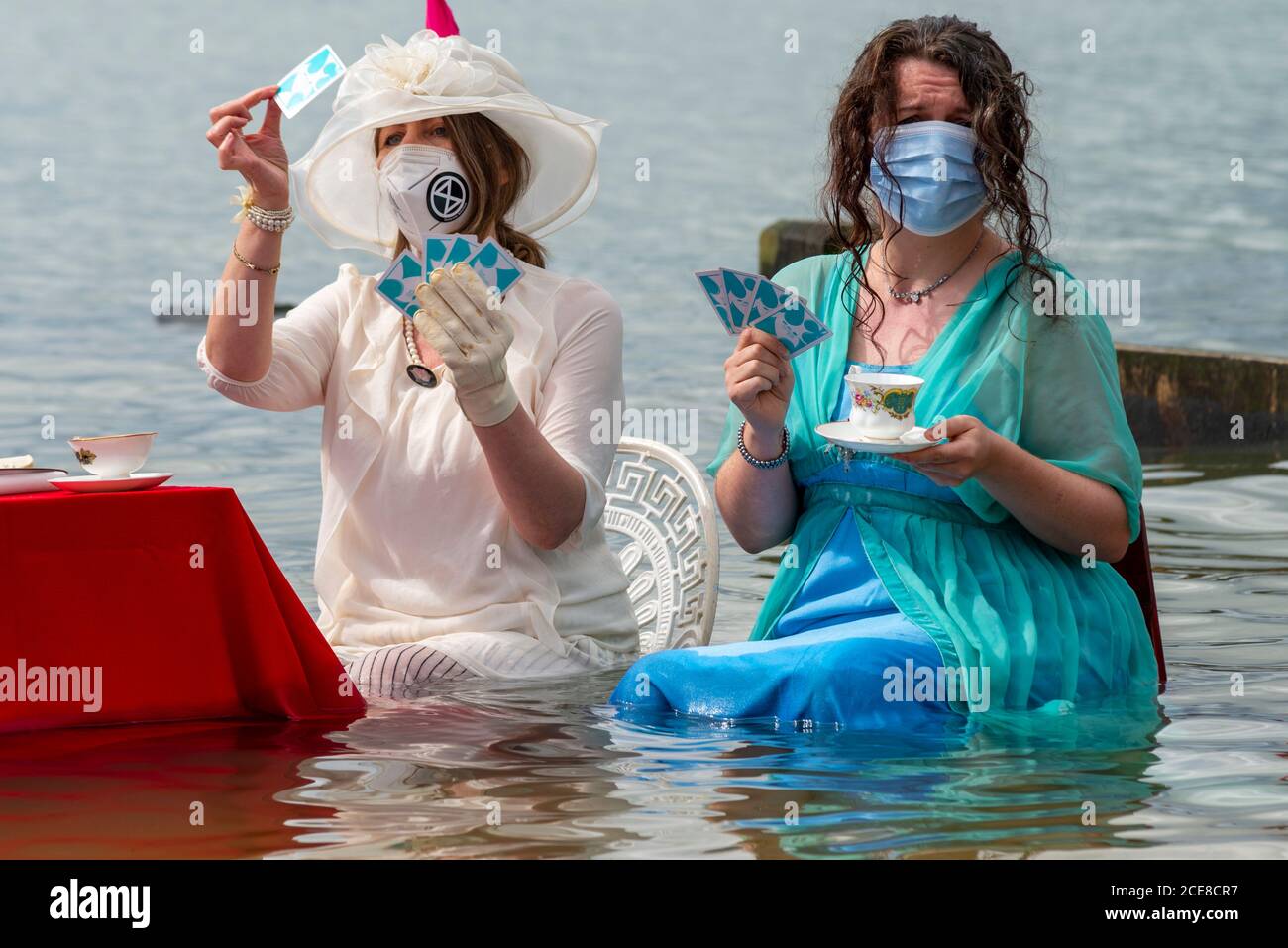 Southend on Sea, Essex, Royaume-Uni. 31 août 2020. La branche locale de la rébellion d'extinction a organisé un événement unique pour symboliser la montée des marées causées par le changement climatique en mettant en place une table dans la mer pour le thé de l'après-midi quand la marée arrive à la station balnéaire. Vêtu d'une tenue d'époque édouardienne, l'idée est de représenter le groupe qui joue comme des éviers Titanic. Deux femelles portant un masque facial, buvant du thé et des cartes à jouer Banque D'Images