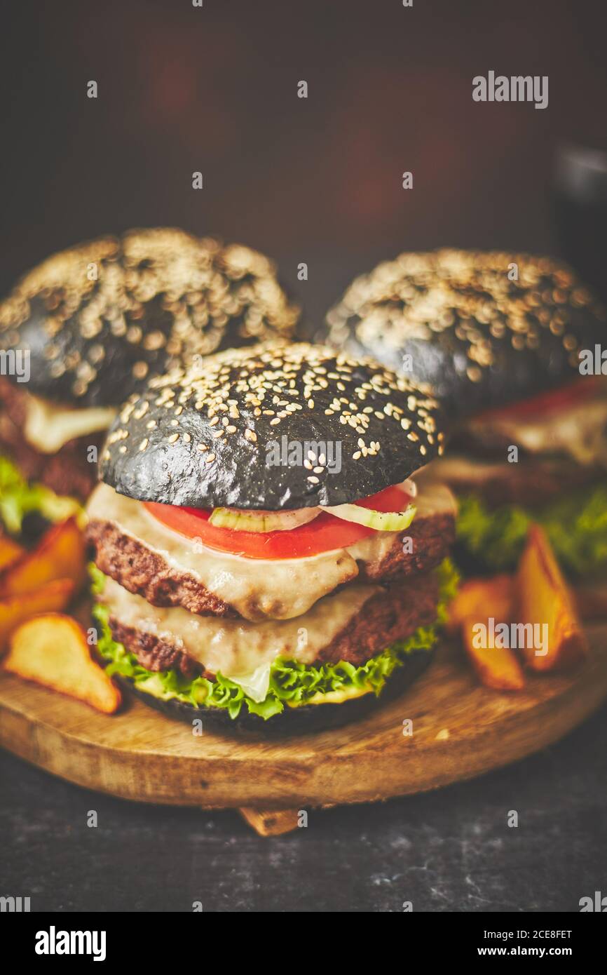 Doubles hamburgers noirs avec fromage. Cheeseburgers japonais avec un petit pain noir sur fond sombre Banque D'Images