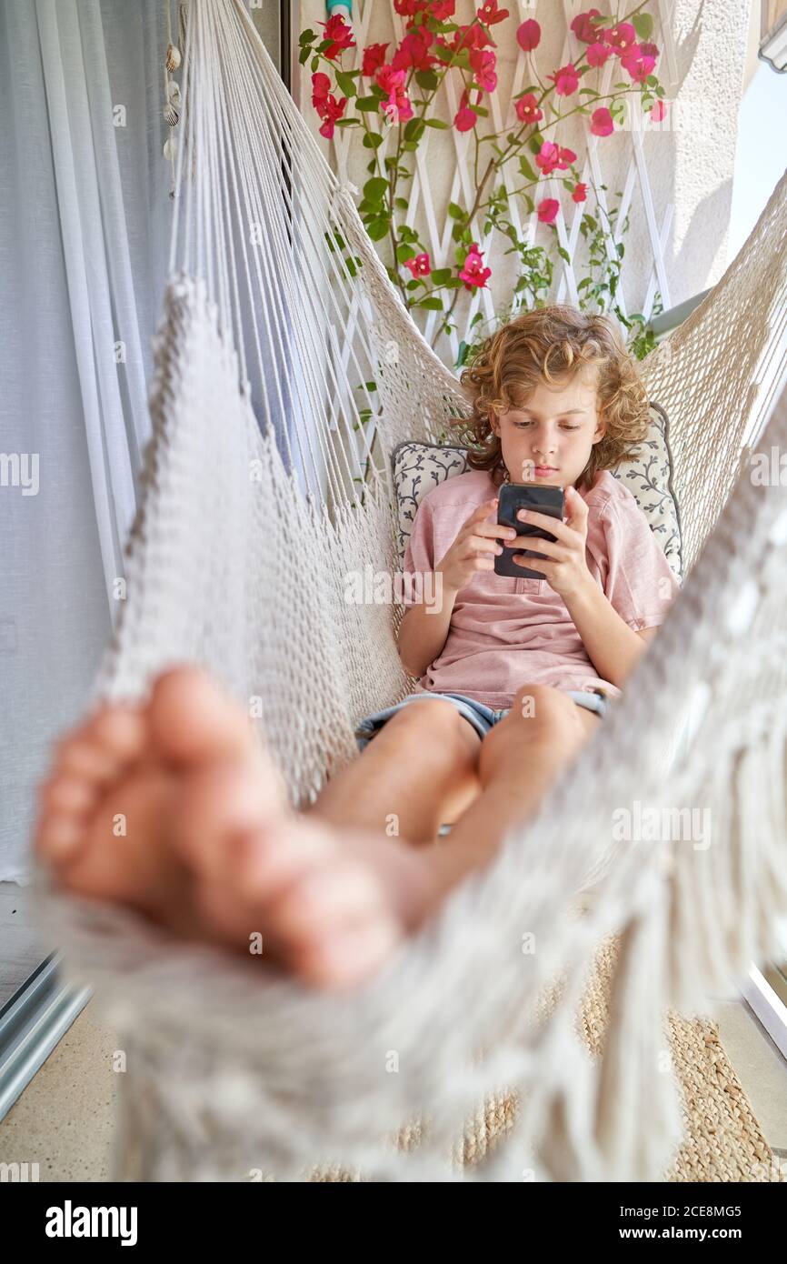 Enfant avec des cheveux bouclés à l'aide d'un téléphone portable lorsqu'il  se repose hamac près de l'usine d'escalade en plein jour Photo Stock - Alamy